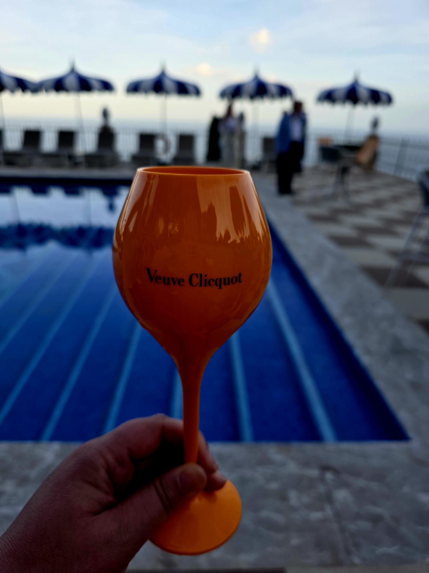 Primo piano di un calice arancione Veuve Clicquot tenuto in mano a bordo della piscina panoramica del Grand Hotel San Pietro a Taormina. Foto di Maria Longo.
